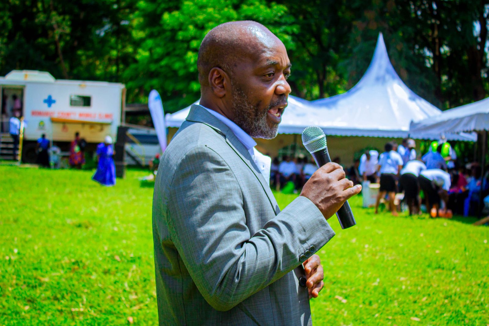 A speaker at a community health gathering beside a Homa Bay County mobile clinic